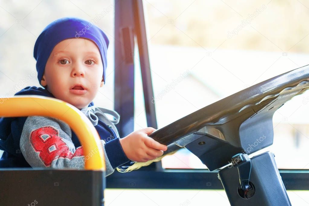 A little boy driving a big bus. The kid plays the driver. Portrait in daylight outdoors