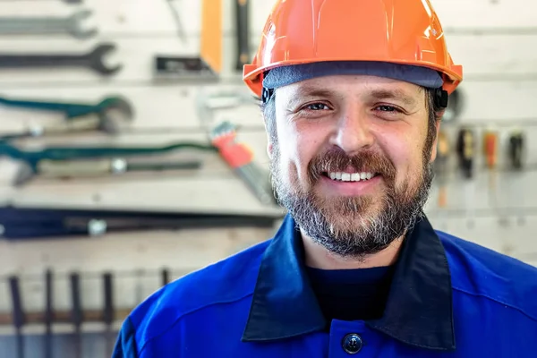 Kask ve iş kıyafetleri içinde bir sakallı bir adam bir stand araçları ile arka planı bembeyaz bir gülümseme gülümsüyor.