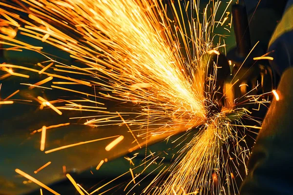 The worker cuts a sheet of metal with a grinder. Fly bright sparks.