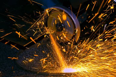 İşçi bir öğütücü ile metal bir parça keser. Parlak kıvılcımlar.