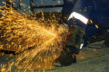 İşçi bir öğütücü ile metal bir parça keser. Parlak kıvılcımlar.