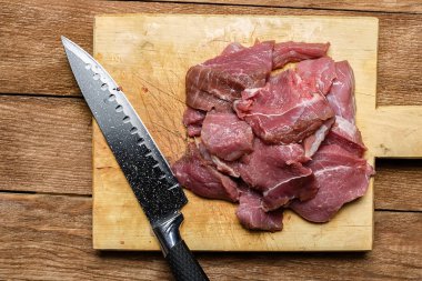 Çiğ et ahşap kesme tahtası siyah bir bıçakla dilim. Lifleri ile sığır eti Close-up. Yukarıdan görüntülemek.