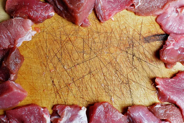 The frame of the pieces of raw meat on a cutting board with scratches and cuts from a knife.