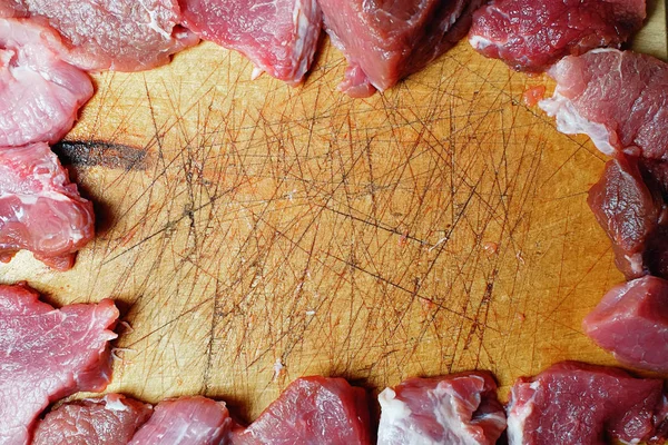 The frame of the pieces of raw meat on a cutting board with scratches and cuts from a knife. Top view with copy space.