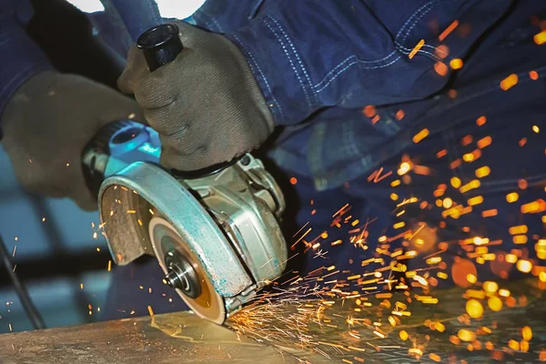 Worker in gloves and an angle grinder cuts a metal sheet. Sparks fly. Close-up of hands with tools during work.