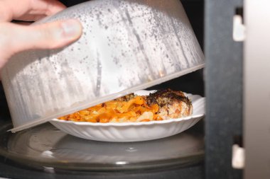 Plaka gıda ile mikrodalga ısıttı. Yararları ve yiyecek için mikrodalga radyasyon tehlikeleri soru. Aşçı ve plastik kapak açılır ve plaka üzerinde öğle yemeği görebilirsiniz.