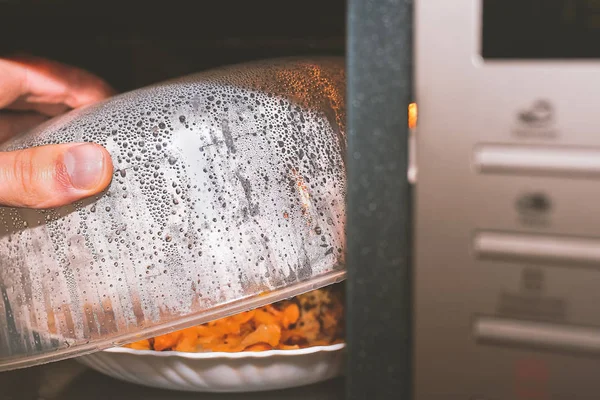 Plaka gıda ile mikrodalga ısıttı. Yararları ve yiyecek için mikrodalga radyasyon tehlikeleri soru. Aşçı ve plastik kapak açılır ve plaka üzerinde öğle yemeği görebilirsiniz.