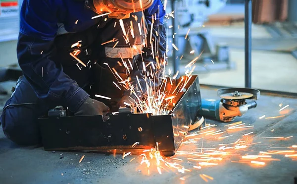 İşçi atölye ve kaynaklı metal parça beton zemin üzerinde oturur. Parlak kıvılcımlar.