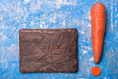 Carrot in the shape of an exclamation mark next to the cutting board. Preparation for writing a menu or recipe for vegans and raw foodists. clipart