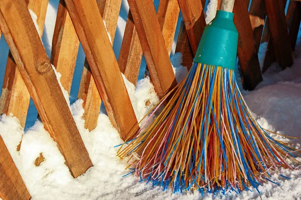 Una escoba de plástico con cerdas multicolores de la pila se encuentra en la nieve. El concepto de limpieza de la zona de nieve en el invierno. Primer plano de un objeto con espacio para copiar . — Foto de Stock