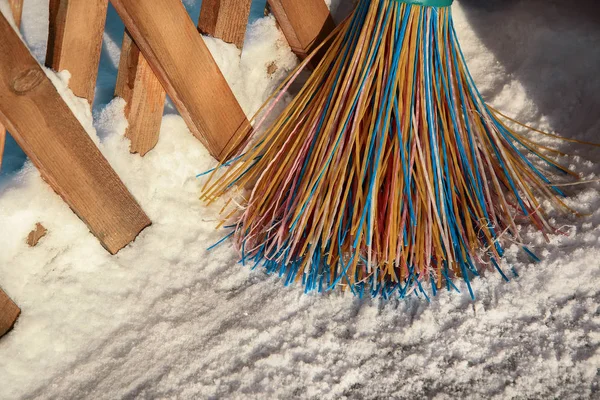 Una escoba de plástico con cerdas multicolores de la pila se encuentra en la nieve. El concepto de limpieza de la zona de nieve en el invierno. Primer plano de un objeto con espacio para copiar . — Foto de Stock