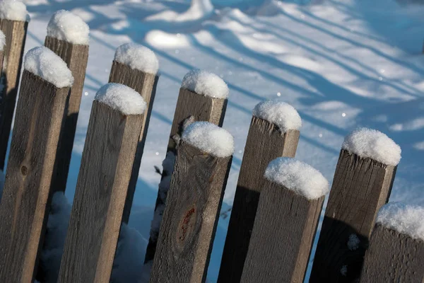 Een houten hek bedekt met sneeuw stokken uit een sneeuwjacht. Ijzige zonnige dag in het dorp. — Stockfoto