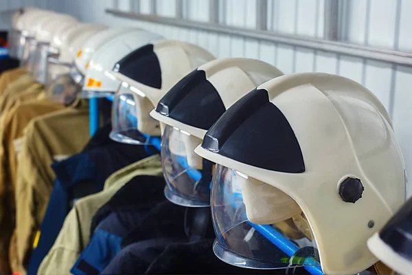 Rescue clothing hanging on hangers. Many helmets of firefighters in a row