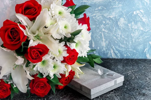 Antecedentes, layout para parabéns às mulheres. Um buquê de flores de rosas, lírios e crisântemos com um presente em uma caixa de prata . — Fotografia de Stock
