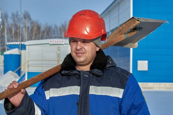 Werknemer in winter overalls en een helm met een schop op zijn schouder. — Stockfoto