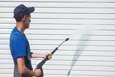 Tulumlu işçi, su tabancası ile yan yana beyaz bir duvarı yıkar