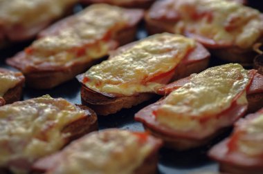 Jambon ve peynir ile birçok pişmiş sıcak sandviç ler bir tepsi üzerinde üst üste yalan.