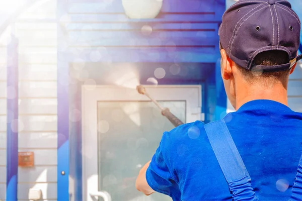 Werknemer in overalls wast een witte muur van een gevel met een waterpistool — Stockfoto