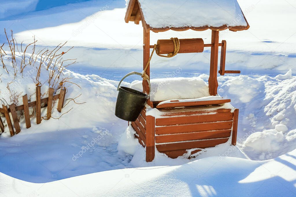 Winter village landscape. A wooden well and a fence in snowdrifts. Its a sunny, frosty day.