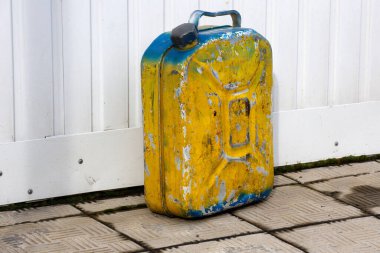 Eski sarı metal bir kutu beyaz bir duvarın karşısında duruyor. Açık bir alanda yanıcı sıvı içeren bir kap