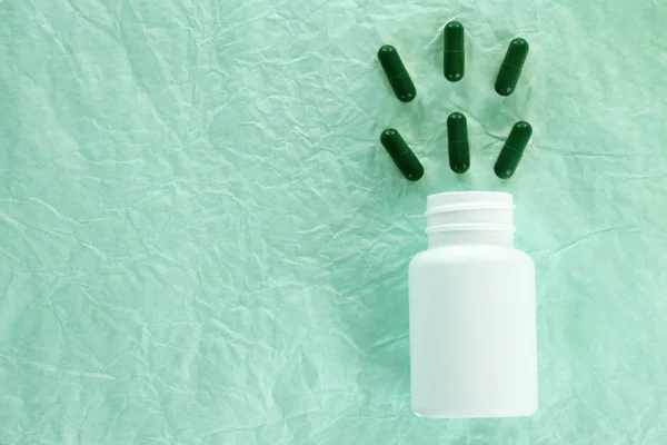 Flat lay composition with green pills flying into white bottle — Stock Photo, Image
