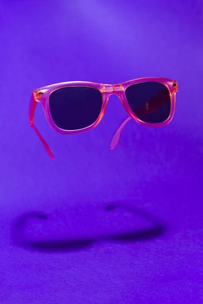明るいピンク色のサングラスを空中に浮揚させます ピンクのサングラスを紫色の背景に浮かぶ メガネの下の低いシャドウ ミニマリズム夏のコンセプト — ストック写真