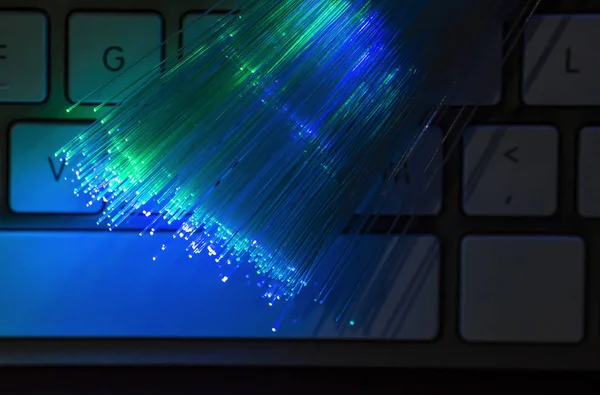 カラフルな光ファイバーがキーボードに点灯します 高速インターネットの概念 データは 光ファイバー ケーブルを転送します さまざまな色に輝く多くの光ファイバーの束 技術の背景 — ストック写真