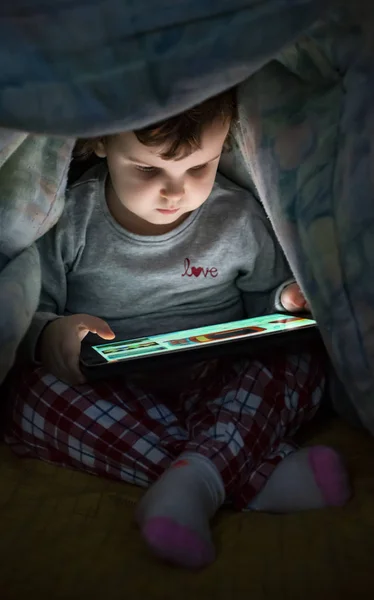 Маленькая девочка смотрит свой планшет в кровати. Иллюминированный ребенок — стоковое фото