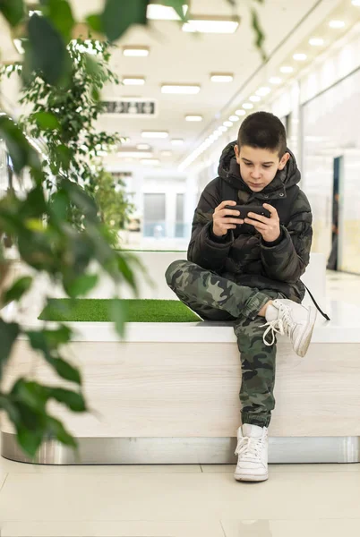 Adolescente jogando com smartphone no centro comercial moderno. Te — Fotografia de Stock