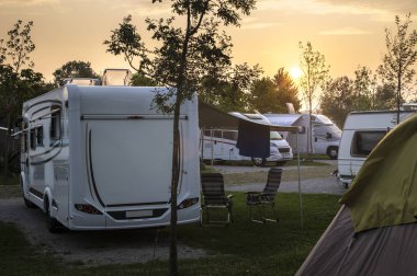 Caravans and campers on green meadow in campsite. Sunrise, rays  clipart