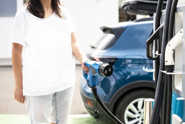 女性はガソリンスタンドで電気自動車を充電します。青い車と電気 — ストック写真