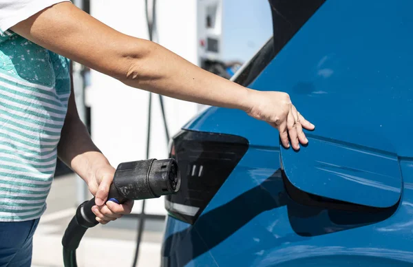 女性はガソリンスタンドで電気自動車を充電します。青い車と電気 — ストック写真