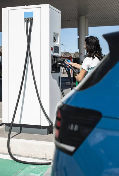 女性はガソリンスタンドで電気自動車を充電します。青い車と電気 — ストック写真