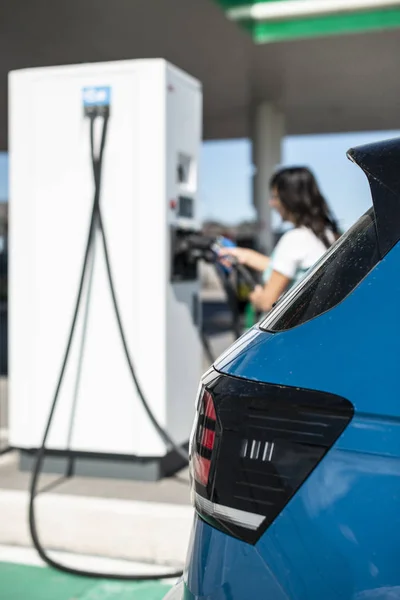 Жінка заряд електричний автомобіль на АЗС. Синій автомобіль і електричний — стокове фото