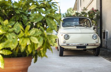 Küçük klasik İtalyan arabası. Eski evin önünde bej rengi eski bir araba ve çiçekler... 