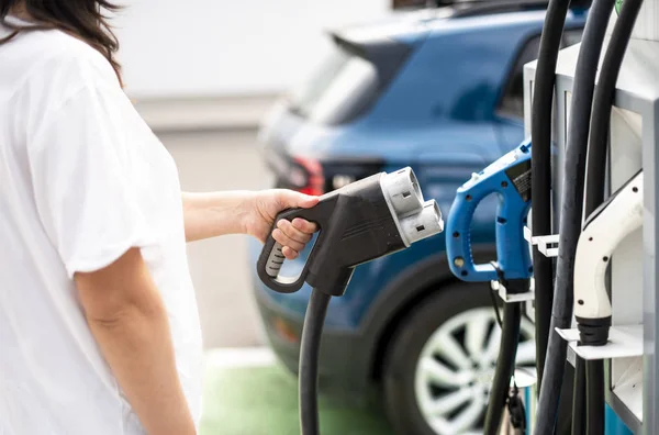 Vrouw opladen elektrische auto op benzinestation. Blauwe auto en elektrische — Stockfoto