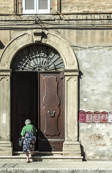 La donna anziana entra in casa. Vecchia porta in legno tipica italiana — Foto Stock