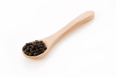 Beyaz zemin üzerinde tahta kaşık olan siyah biber.