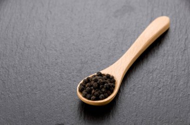 Kara biberli tahta kaşık. Siyah taş tabakta.