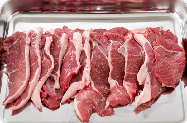 Raw lamb meat on a stainless steel tray on white background.