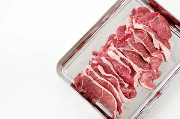 Raw lamb meat on a stainless steel tray on white background.