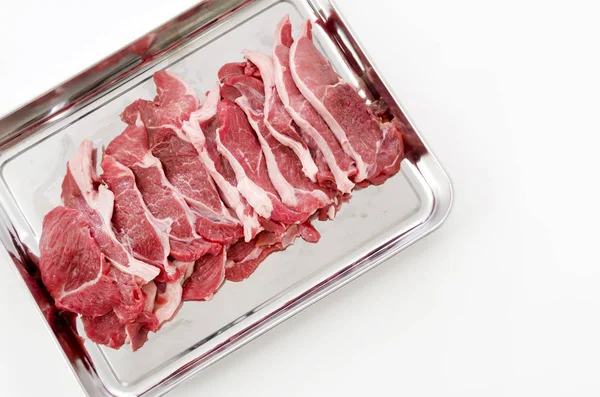 Raw lamb meat on a stainless steel tray on white background.