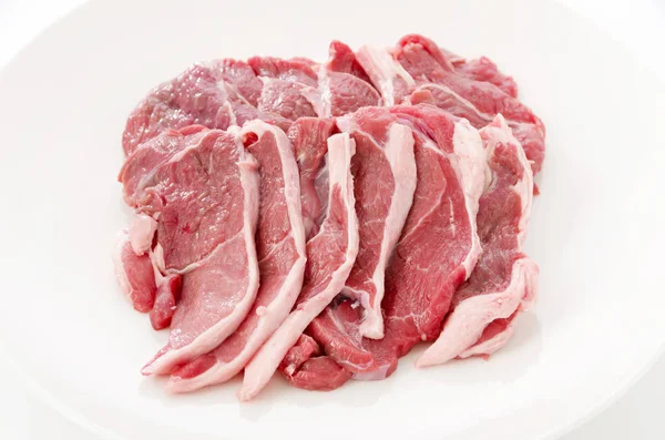 Raw lamb meat on a white plate on white background