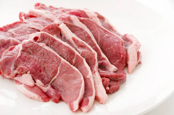 Raw lamb meat on a white plate on white background
