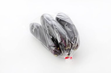 Beyaz arka planda plastik poşette çiğ siyah patlıcan.
