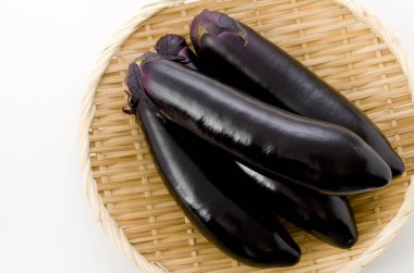 Beyaz arka planda bambu elek üzerinde ham siyah patlıcan.