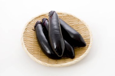 Beyaz arka planda bambu elek üzerinde ham siyah patlıcan.