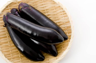 Beyaz arka planda bambu elek üzerinde ham siyah patlıcan.