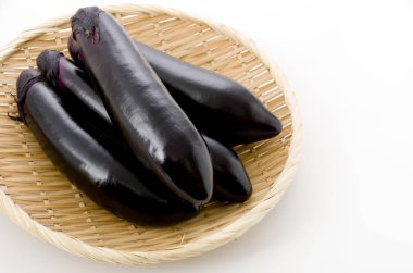 Beyaz arka planda bambu elek üzerinde ham siyah patlıcan.