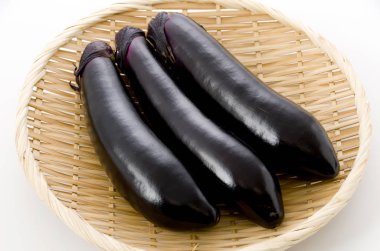 Beyaz arka planda bambu elek üzerinde ham siyah patlıcan.